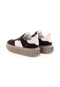 Bruine en witte sneaker van suede en leer, met een stevige beige rubberen zool en contrasterende kleuraccenten. Voorzien van een trekhaak en vetersluiting.