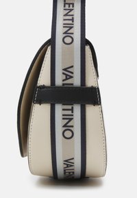 Borsa beige con design strutturato, dotata di una tracolla nera con strisce bianche e blu navy, con il nome del brand in evidenza.
