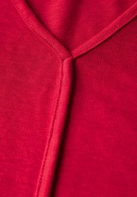 Tela roja con una textura suave, que presenta un diseño de escote en V y una costura precisa a lo largo del escote. No se observan patrones ni herrajes.