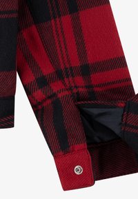 Manche de chemise en flanelle à carreaux rouge et noir avec une fermeture à bouton. Le tissu présente une texture douce et un motif tissé.
