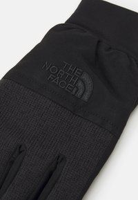Gants noirs avec un design en tricot texturé sur la partie inférieure et un tissu lisse sur la partie supérieure, ornés du logo "THE NORTH FACE".