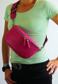Fuchsia leren crossbody tas met ritsluiting en dubbele ritslokken; verstelbare zwarte en roze gestippelde schouderband; semi-rigide vorm.