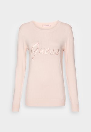 Pull rose clair à manches longues avec col rond, arborant le logo "Guess" en écriture cursive orné de petites pierres décoratives sur la poitrine.