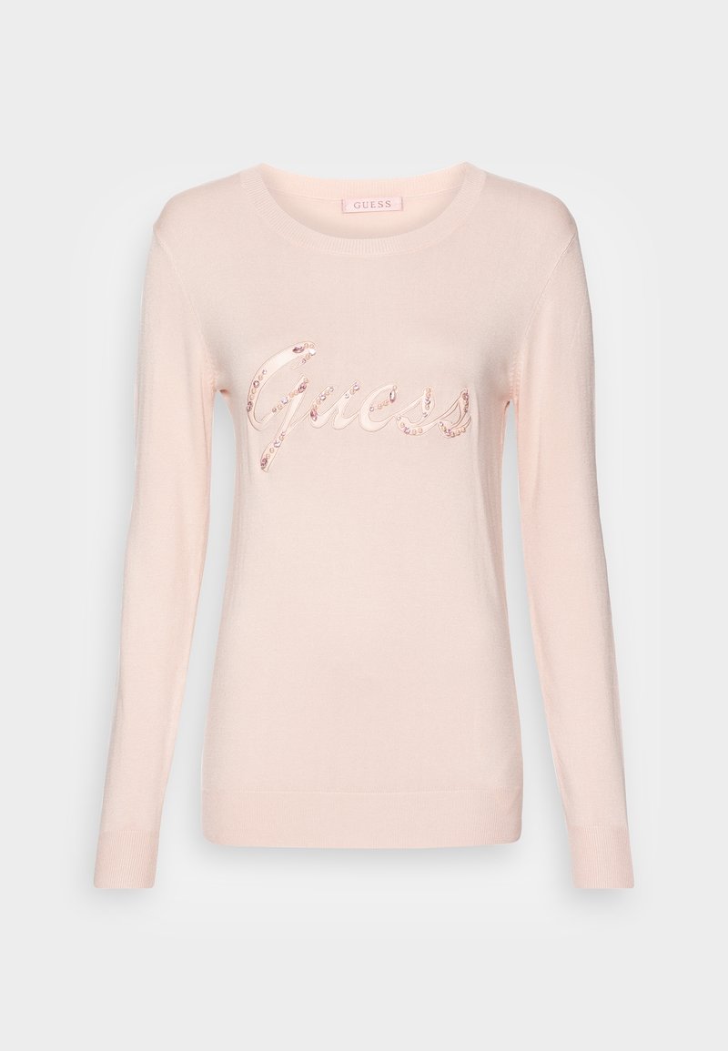 Pull rose clair à manches longues avec col rond, arborant le logo "Guess" en écriture cursive orné de petites pierres décoratives sur la poitrine.