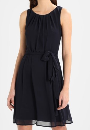 Marineblauwe mouwloze jurk met een ronde hals, geplooid stof bij de buste, een getailleerde taille en een strikdetail in de taille, zachte textuur.