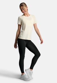Light yellow short-sleeve shirt, black leggings, and white sneakers. Smooth fabric, fitted tapering leggings, subtle seam details.