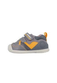 Zapato para niño pequeño en gris y amarillo con dos correas de Velcro ajustables, suela de goma, acentos cosidos y parte superior de tela texturizada.