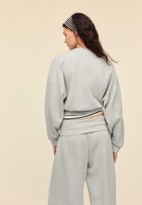 Grauer Pullover mit übergroßem Schnitt, gerippten Bündchen und einem schwarz-weiß gestreiften Bund. Kombinieren Sie ihn mit grauen Hosen mit weitem Bein.