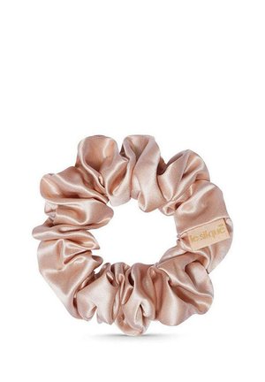 Lichtroze satijnen scrunchie met een klein beige label op een witte achtergrond, met een gladde, glanzende stof en geraffineerde textuur.