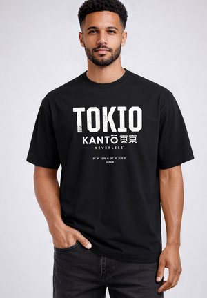 Mann mit kurzen lockigen Haaren und Bart, der ein schwarzes T-Shirt mit weißem Text "TOKIO KANTO NEVERLESS" und geografischen Koordinaten trägt.