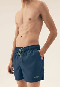 Granatowe szorty do pływania z elastycznym pasem, zielonym sznurkiem w talii i kieszeniami bocznymi. Miękki, lekki materiał z logo na dolnej części przodu.