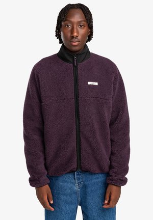 Fleece jacket in dark purple with a high black collar and front zip. Features a textured surface and a small label on the chest.