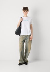 Hvit bomull T-skjorte med turkise "Calvin Klein"-bokstaver. Lyseblå jeans med slitt utseende. Svart lærveske. Svarte flate sko.