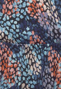 Mehrfarbiger Stoff mit dunklem Hintergrund, der ein Muster aus abstrakten Formen in Blau, Koralle und Hellrosa zeigt. Elastischer Taillendetail sichtbar.