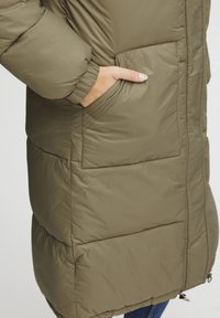Doudoune vert olive avec poches latérales, poignets côtelés et motif en matelassé. Présente une coupe décontractée et un ourlet ajustable avec cordon.