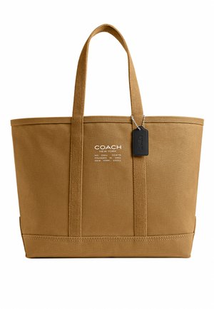 Bolso tote marrón de Coach con dos asas, texto de logo blanco en la parte delantera y etiqueta de cuero negra colgando del asa derecha.