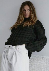 Czarny sweter dziany o żebrowanej strukturze, luźnym kroju i szerokich rękawach, zestawiony z białymi spodniami z wysokim stanem z plisami.