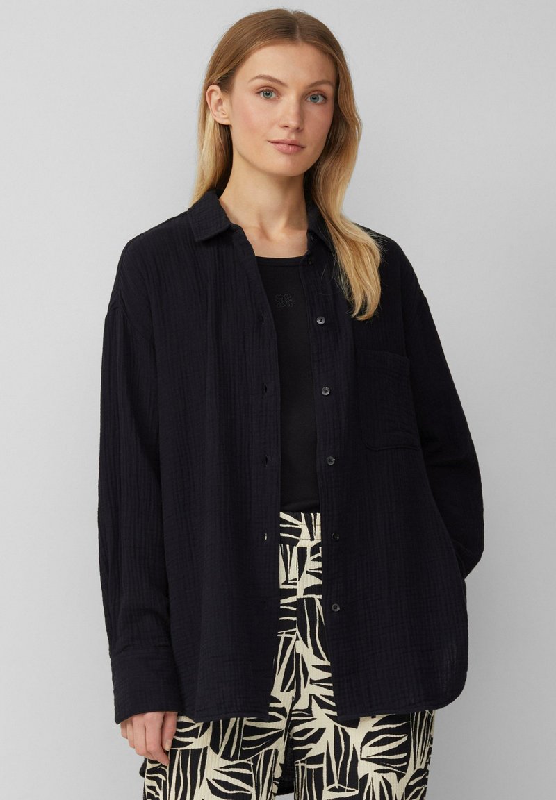 Zwarte textuurshirt met een knoopsluiting aan de voorkant, lange mouwen en een borstzak, gecombineerd met gestreepte crèmekleurige en zwarte broek.