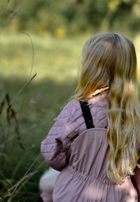 Paminkštinta rausva su pūtomis siūlėmis striukė su aukštu apykakliu, juodomis juostelėmis ir ilgi blondinų plaukai, fone matyti neryškus gamtos peizažas.