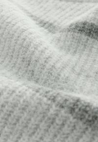 Lichtgrijze gebreide stof met een zachte, getextureerde oppervlakte. Voorzien van subtiele geribbelde patronen en een licht pluizige uitstraling.