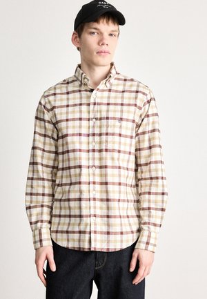 Beige kockás ing bordó, sárga és fehér csíkokkal, gombos gallérral, hosszú ujjakkal és mellsz zsebbe. Sötét farmernadrággal viselve.