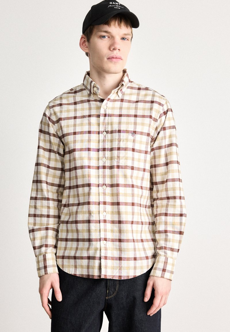 Camicia a quadri beige con striscie color bordeaux, gialle e bianche, colletto button-down, maniche lunghe e taschino sul petto. Indossata con jeans scuri.