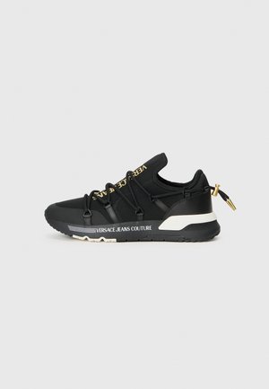 Baskets de sport noires au design épuré, avec un marquage doré, des lacets élastiques et une semelle texturée avec des accents blancs.