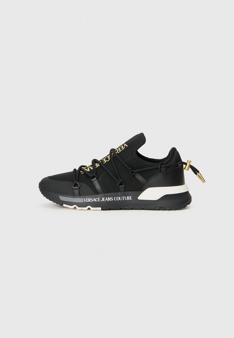 Baskets de sport noires au design épuré, avec un marquage doré, des lacets élastiques et une semelle texturée avec des accents blancs.