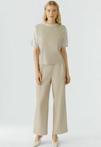 Beige top met korte, gestructureerde mouwen en subtiele logo-details; gecombineerd met bijpassende wijde broek. Gladde stof met een strak uiterlijk.