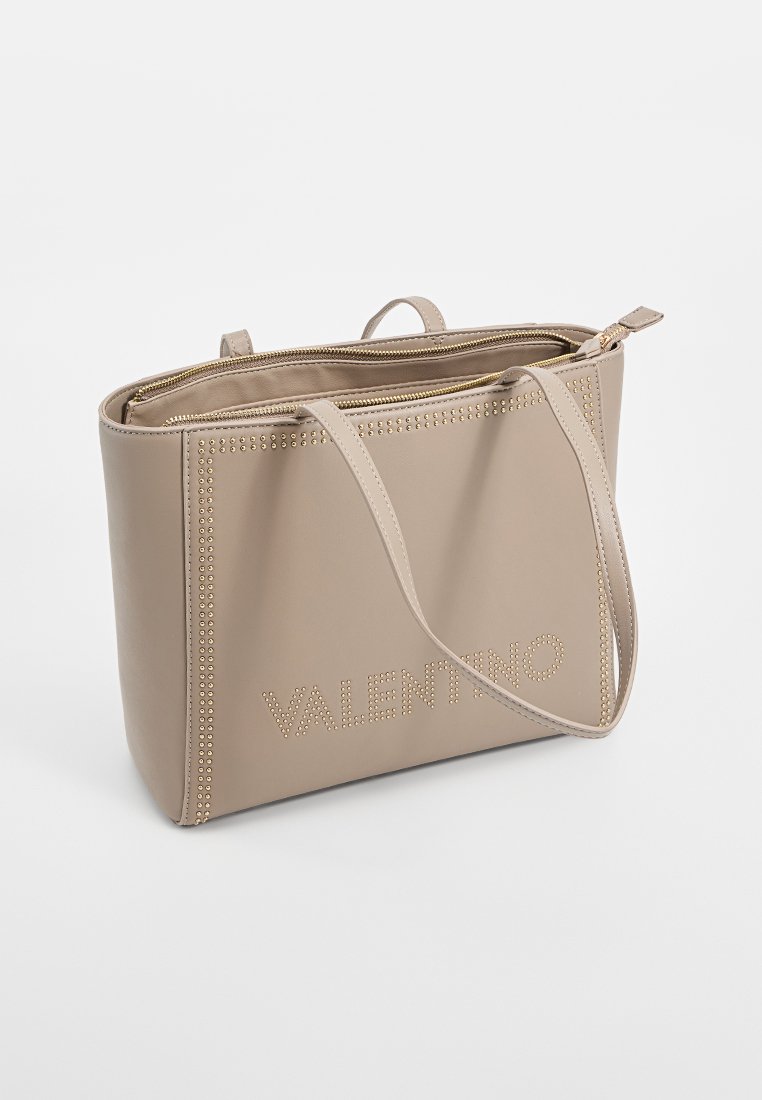 Bolso tote de cuero beige con acentos de tachuelas y cierre con cremallera. La parte frontal presenta un logotipo en relieve y tiene dos asas para el hombro.