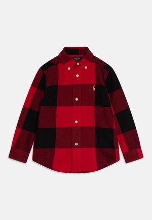 Camisa de botones de manga larga con cuadros rojos y negros, con cuello y pequeño logo bordado amarillo en el pecho izquierdo.