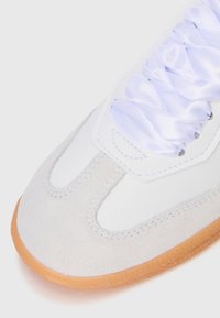 Hvit sneaker med glatt skinn, semsket detaljer, rund form, lyse lilla satinsnører og en brun gummisåle.