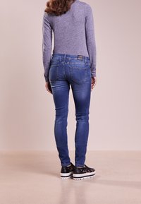 Vaqueros pitillo de mezclilla azul con cintura alta, cinco bolsillos y acabado texturizado. Combinados con zapatos negros tipo slip-on con estampado de leopardo.