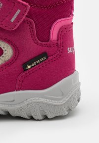 Dziecięce buty trekkingowe w jaskrawym różowym zamszu z szarą gumową podeszwą. Posiadają etykietę Gore-Tex, teksturowaną cholewkę oraz wspierający pasek.