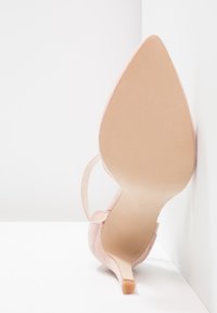 Rosa högklackad sko med spetsig tådesign, slät mockamaterial och smal klack. Ljusfärgad sula och minimalistiska remdetaljer.