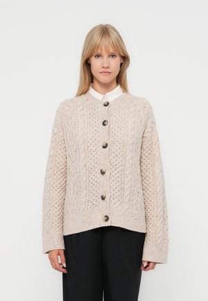 Strikket cardigan i lys beige med teksturerte kabelmønstre og store mørke knapper, med en avslappet passform og ribbede mansjetter.