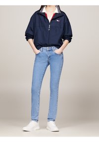 Cortavientos navy con cuello a rayas blancas y rojas, combinado con jeans skinny azul claro y zapatillas blancas, creando un atuendo casual.