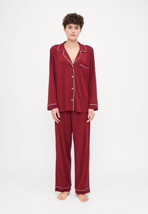 Burgundy pajama set with a button-up long-sleeve top featuring white piping, paired with loose-fitting, matching pants. Soft fabric texture.