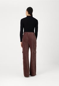 Καφέ παντελόνι cargo από κορτούρα με φαρδιά πόδια, με πλαϊνές τσέπες και ελαστική ζώνη, σε συνδυασμό με ένα στενό μαύρο μπλούζα με μακρύ μανίκι.