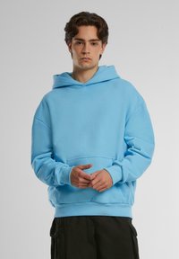 Felpa con cappuccio di colore azzurro chiaro realizzata in tessuto morbido. Presenta una tasca a marsupio e polsini a costine. Vestibilità morbida con un design classico.