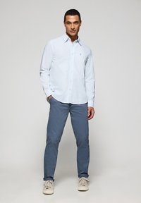 Ljusblå långärmad skjorta med knappar och en liten logotyp, tillsammans med ljusgrå-blå byxor och beige sneakers. Enkelt design, skräddarsydd passform.