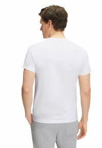 Maglietta bianca a maniche corte con scollo rotondo. Tessuto morbido, design aderente e stile minimalista. Indossata con pantaloni grigi.