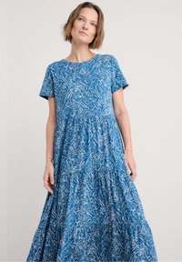 Robe maxi à motifs floraux bleus, avec manches courtes, col rond et jupe à volants. Fabriquée dans un tissu léger au toucher doux.