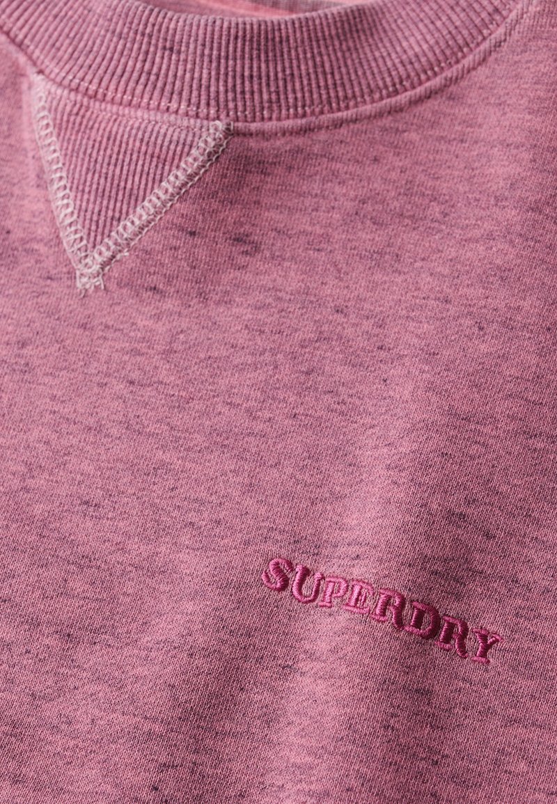 Felpa rosa con colletto a costine e dettagli sulle spalle. Presenta il nome del marchio "SUPERDRY" ricamato in rosa scuro sul petto.