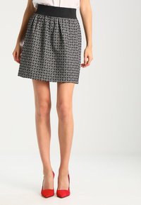 Schwarz-weiß gemusterter Rock mit einem plissierten Design, breitem elastischen Bund und knielanger Schnitt, kombiniert mit roten High Heels.