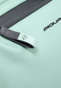 Mochila verde menta con un zipper y asa negros. Presenta un logotipo sutil y una textura suave y resistente al agua.