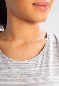 Top grigio a righe con scollatura rotonda e texture morbida, posizionato su uno sfondo neutro, che mette in risalto la zona del collo e il tessuto liscio.