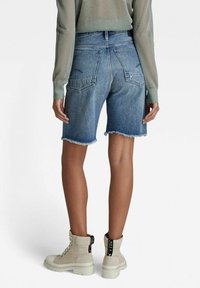 Shorts de mezclilla en azul claro con bordes deshilachados y bolsillos traseros. Combinados con botas de tobillo beige que tienen cordones negros y etiquetas.