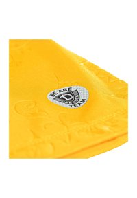 Tissu jaune avec un motif texturé, comportant une patch logo argenté portant l'inscription "NOUS SOMMES L'ÉQUIPE DRESDEN." Des accents incluent un éclat subtil.