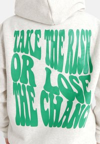 Sudadera gris con un llamativo texto gráfico en verde en la parte posterior: "TOMA EL RIESGO O PIERDE LA OPORTUNIDAD." Textura suave, corte relajado.
